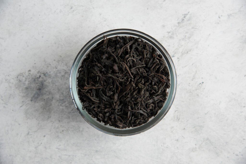 a glass bowl with dry tea leaves on a marble background
