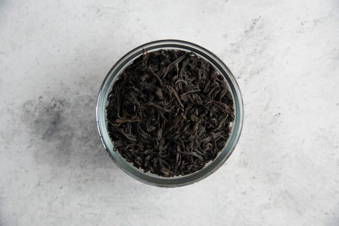 a glass bowl with dry tea leaves on a marble background